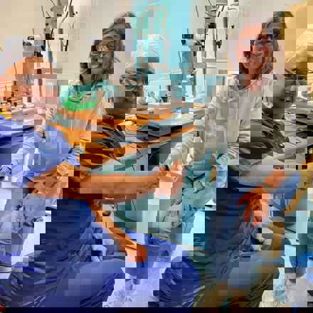 Angela Young, a white female in her early 60s in eye clinic shaking hands with consultant ophthalmologist. Both smiling and looking to camera