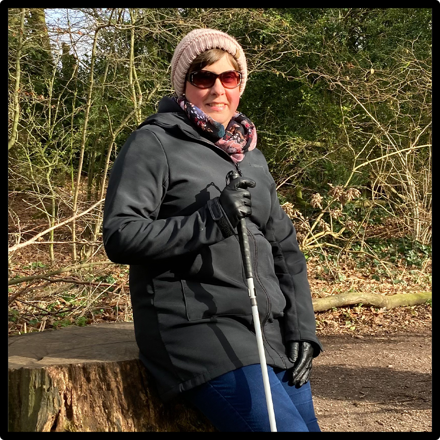 Louise smiling at the camera in the woods holding a cane