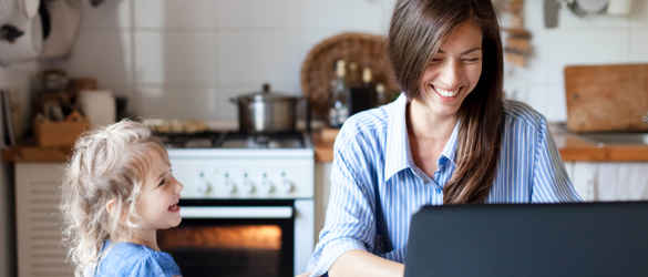 Mother and young daughter on laptop in kitchen laughing