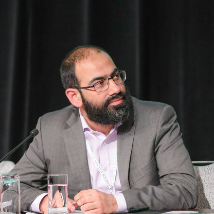 Omar Mahroo. He has dark hair and a beard. He is wearing glasses and a grey suit. 