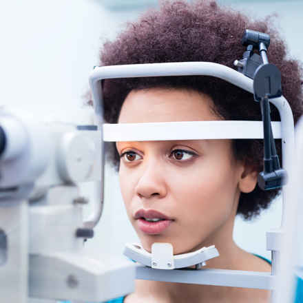 Woman having eye test, resting forehead and chin against machine.