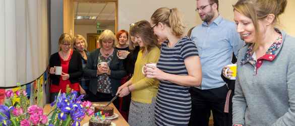 Staff smiling as they cut cake